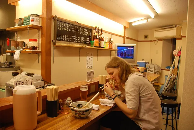 Eating ramen in Dotonbori, Osaka. An actual ramen-eating scene photographed in Dotonbori, Osaka. Eating is shown as a comfortable personal action, not a performance visitors are required to imitate.